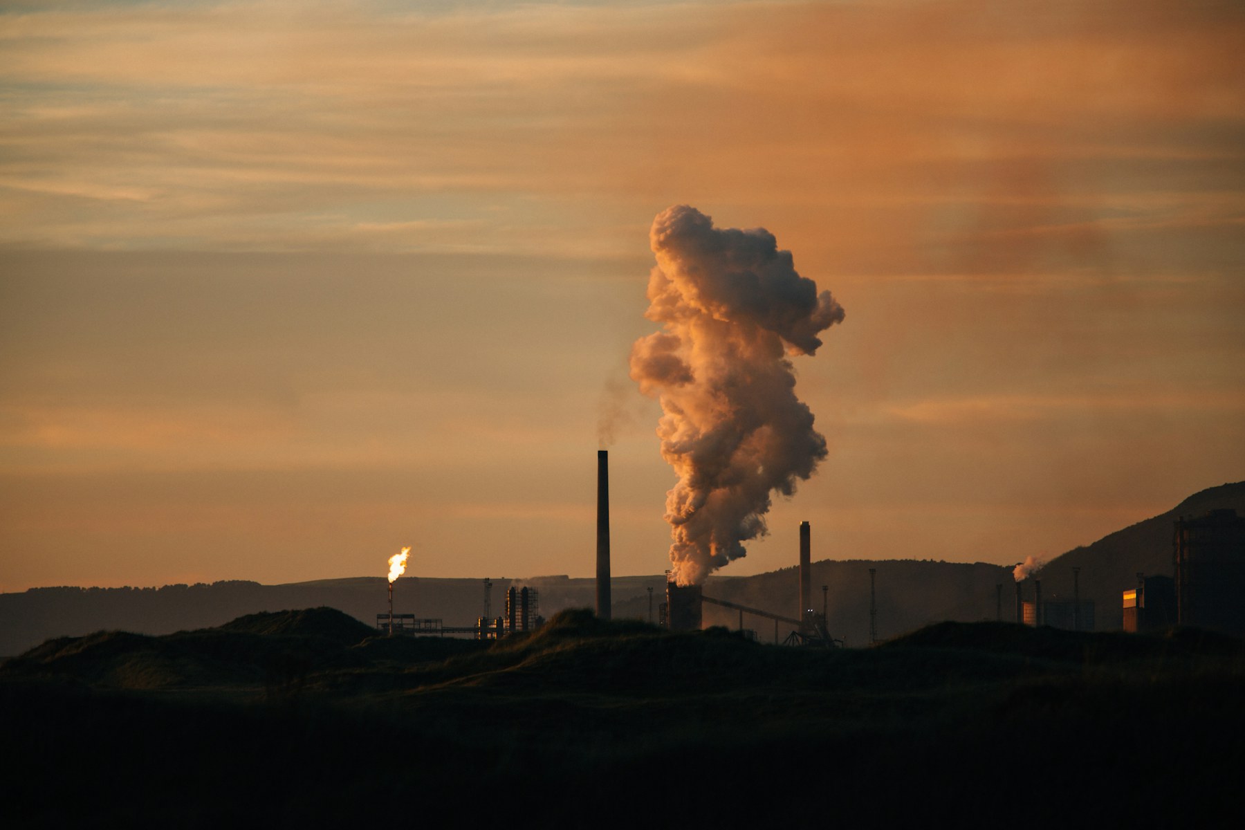 Industrial plant at sunset, smoke billowing against a peach sky